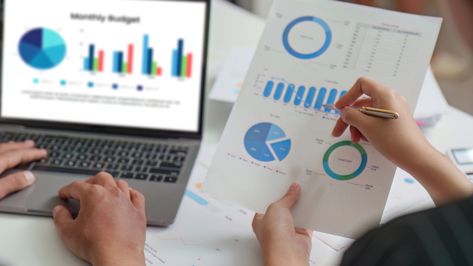 Two people analyzing financial charts and IT budget data on laptop and paper